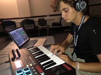 a young man playing an electronic keyboard in front of a laptop